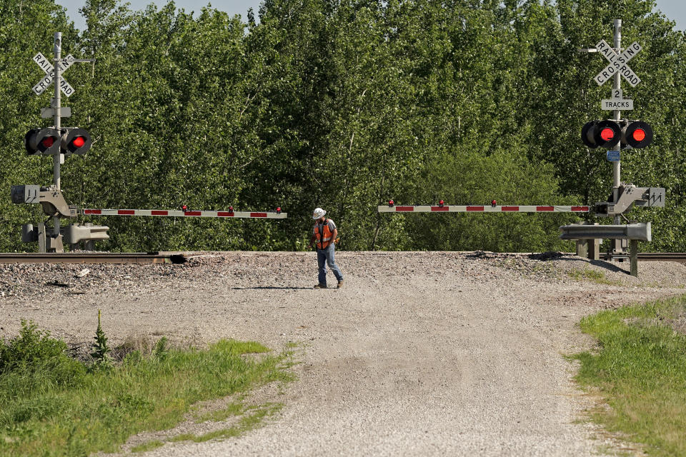 A worker stands at a crossing Tuesday, June 28, 2022, a mile west of the crossing near Mendon, Mo., where an Amtrak train derailed after striking a dump truck Monday. Several people were killed, including the driver of the truck, and others were injured in the wreck. (AP Photo/Charlie Riedel)