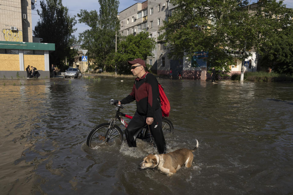 A local resident with a bike and a dog walks along the street past the buildings in Kherson, Ukraine, Tuesday, Jun 6, 2023 which were flooded after the Kakhovka dam was blown up overnight. The wall of a major dam in a part of southern Ukraine has collapsed, triggering floods, endangering Europe's largest nuclear power plant and threatening drinking water supplies. (AP Photo/Evgeniy Maloletka)