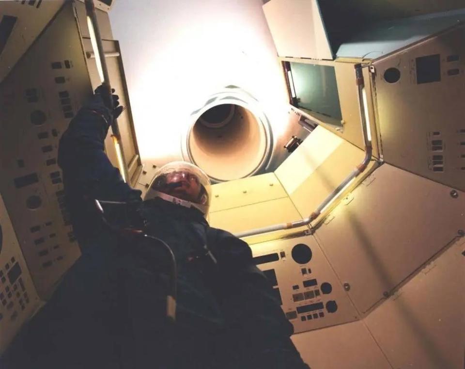 A suited crewmember in a mockup of the MOL crew cabin showing the narrow tunnel leading to the Gemini-B capsule.