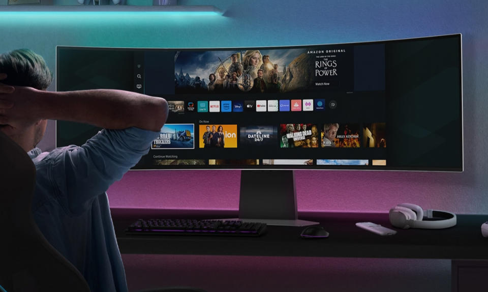 Product lifestyle image of a young man with his arms behind his head looking at an ultra-wide monitor.