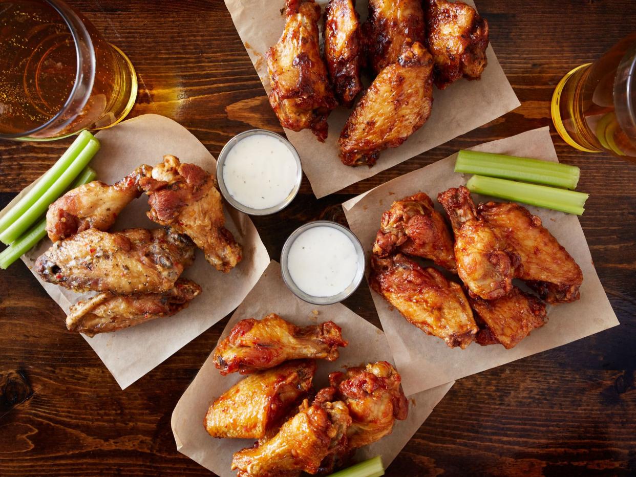 overhead view of four different flavored chicken wings with ranch dressing, beer, and celery sticks