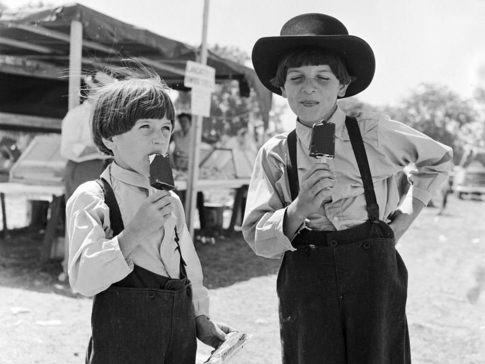 Two Amish boys wearing traditionally plain clothing enjoying ice cream at a local country fair