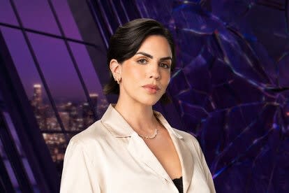 Katie Maloney wearing a white jacket with a black tank top in a purple room overlooking LA.