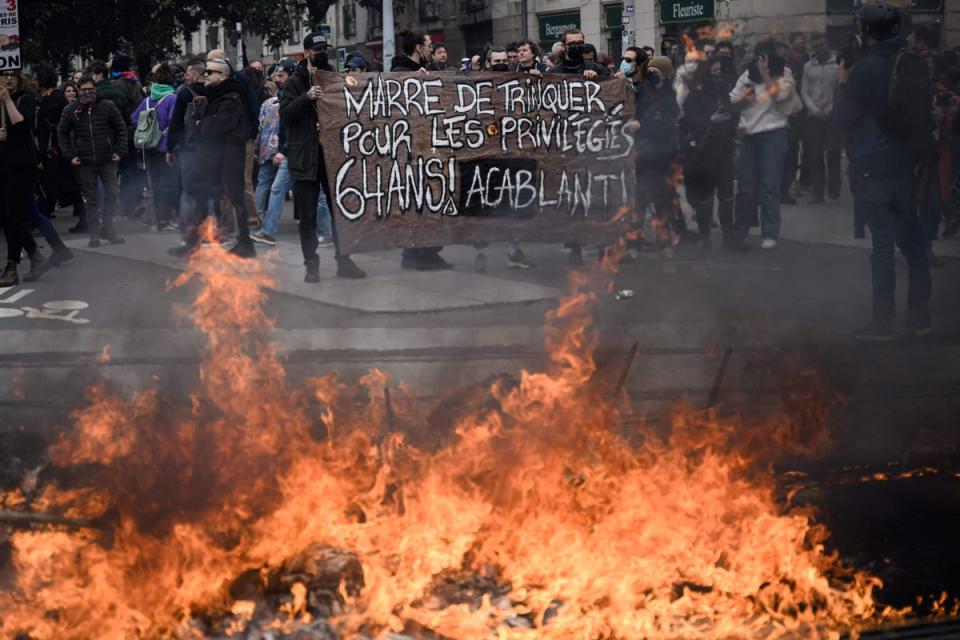 d reading “We are tired of paying for privileged people” as a fire burns during a rally on a nationwide action day, a week after the government pushed a pensions reform through parliament without a vote, using the article 49.3 of the constitution, in Nantes, western France (AFP via Getty Images)