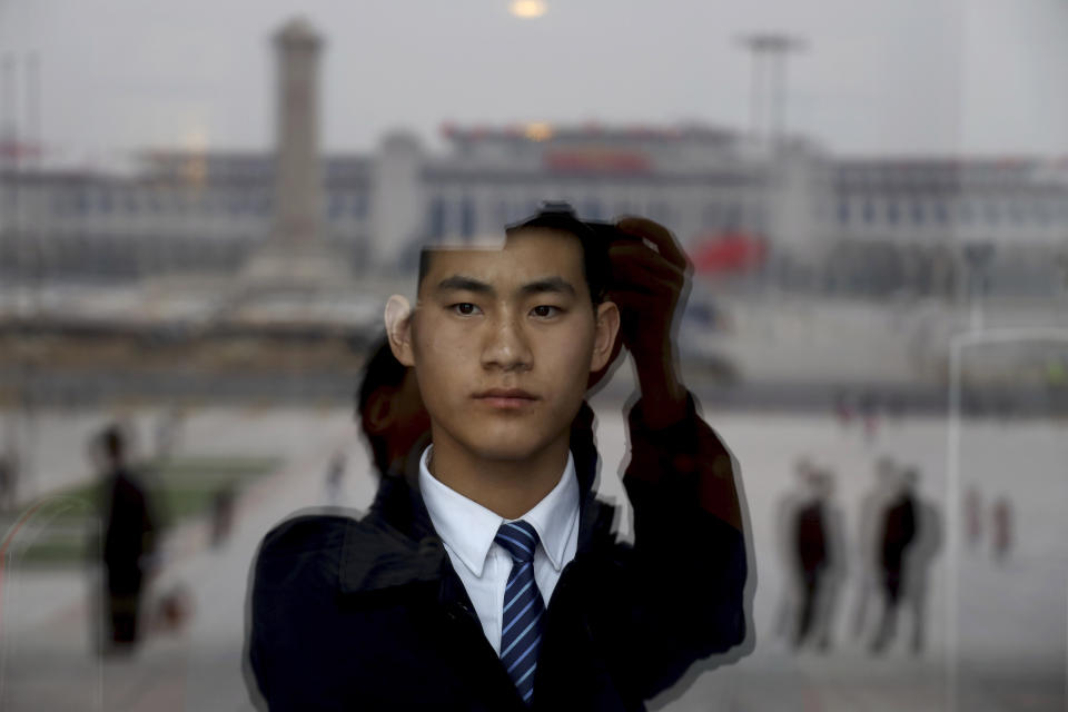 In this March 9, 2019, photo, a security officer stands on duty behind a glass window reflecting Tiananmen Square at the Great Hall of the People where a session of the Chinese People's Political Consultative Conference is held in Beijing. (AP Photo/Ng Han Guan)