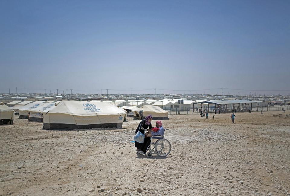 In this Thursday April 17, 2014 photo, a Syrian woman hands her baby to a man in a wheelchair at Zaatari refugee camp, near the Syrian border in Jordan. Life in this sprawling camp, Zaatari, is only getting harder for 130,000 residents, most of them fleeing fighting in south Syria. Security has become hard to control. Earlier this month, an angry mob of refugees attacked Jordanian police, throwing rocks, prompting police to fire tear gas, and there were reports of live ammunition in fighting that left one refugee dead and 28 police wounded. The angry protests were sparked after police detained a family of refugees and a driver who tried to smuggle them out of the camp.(AP Photo/Khalil Hamra)