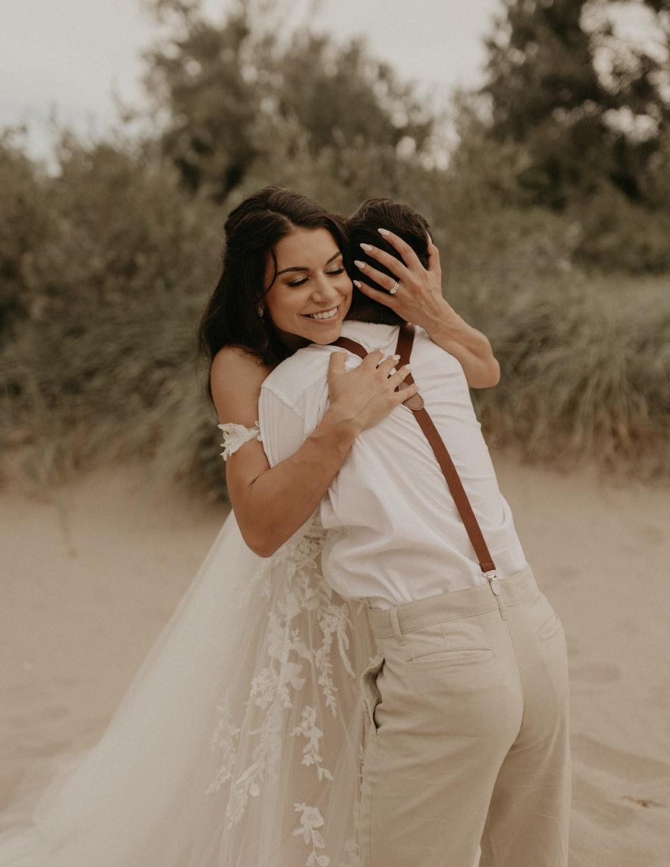 A bride hugs her brother on a beach.