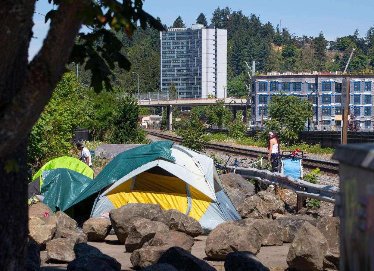 Campers on July 12 occupy a strip of land along the railroad tracks in Eugene as a row of new housing rises in the background near Downtown Riverfront Park.