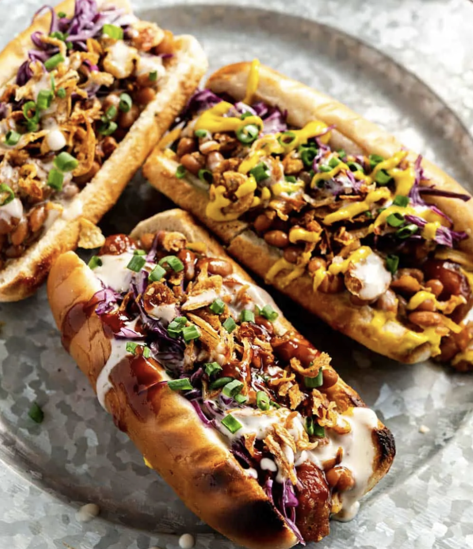 three vegan hot dogs with onions, scallions, cabbage, baked beans, and sauce all over the top