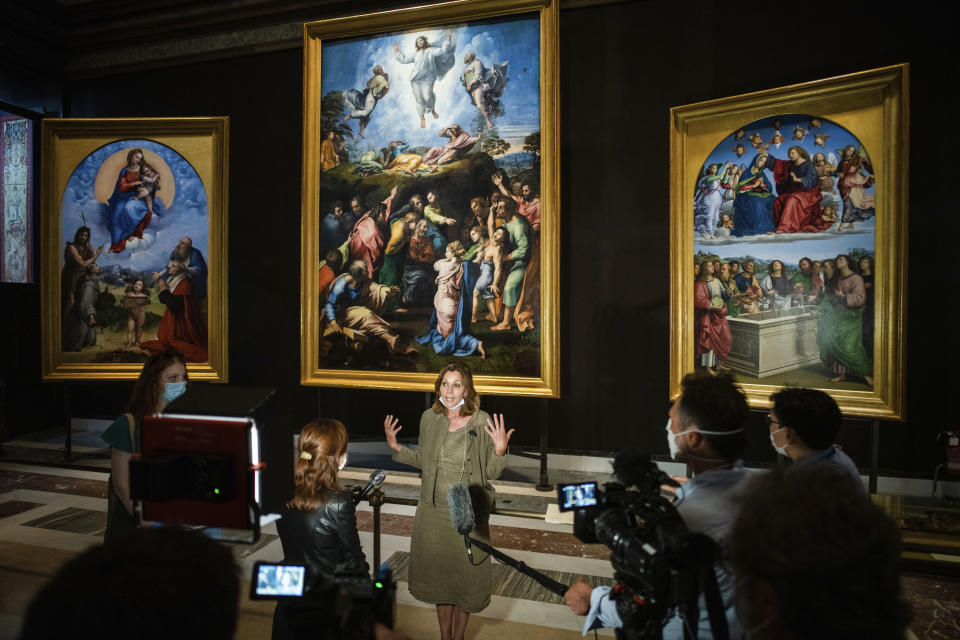 Vatican Museums Barbara Jatta speaks to the media as she stands in front of Raphael's oil on canvas altarpieces, from left, the Madonna of Foligno, the Transfiguration, and the Incarnation of the virgin, at the Vatican Museums, Wednesday, May 3, 2020.The Vatican Museums announced last month that after restorations they have determined that two of the female figures in the Hall of Constantine were oil painted by Raphael himself and not by his worship. (AP Photo/Domenico Stinellis)