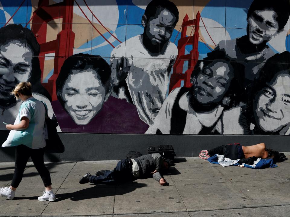 A woman walks past men passed out on the sidewalk n the Tenderloin area of San Francisco, California, U.S., February 28, 2020. Picture taken February 28, 2020. REUTERS:Shannon Stapleton .JPG