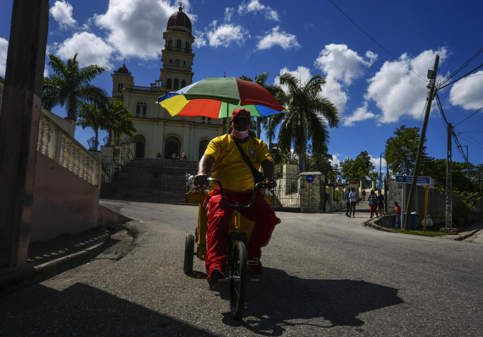 A street vendor rides his bicycle outside the shrine of the Virgin of Charity of El Cobre in El Cobre, Cuba, Sunday, Feb. 11, 2024. The Vatican-recognized Virgin, venerated by Catholics and followers of Afro-Cuban Santeria traditions, is at the heart of Cuban identity, uniting compatriots from the Communist-run Caribbean island to those who were exiled or emigrated to the U.S. (AP Photo/Ramon Espinosa)