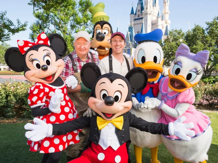Minnie, Mickey, Goofy, Donald and Daisy Duck and two men pose together.