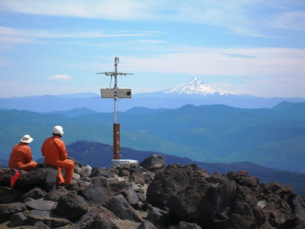 Karl Hagel and Pat McChesney, field engineers with the Pacific Northwest Seismic Network team at the University of Washington, install earthquake monitoring equipment on the slopes of Mount St. Helens, with Mount Hood visible in the distance. (UW / PNSN Photo / Marc Biundo)