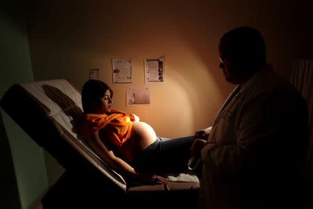 Noriany Rivera, who is 40 weeks pregnant, looks at her belly as she listens to a doctor during a routine check up, as flyers explaining how to prevent Zika, Dengue and Chikungunya viruses are posted on the wall, at a public hospital in San Juan, Puerto Rico, February 3, 2016. REUTERS/Alvin Baez/File Photo