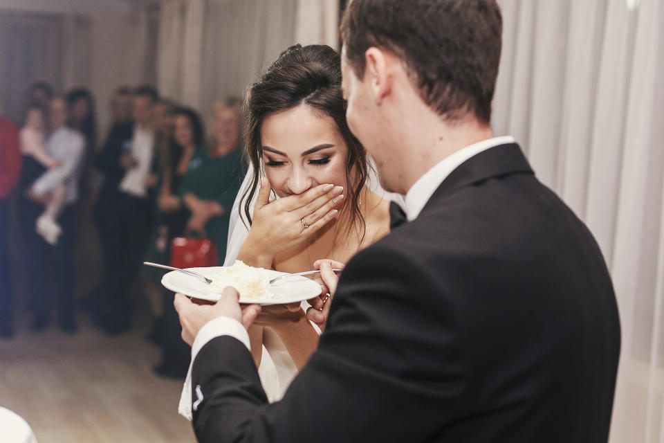 gorgeous bride and stylish groom tasting their stylish wedding cake at wedding reception in restaurant. happy newlywed couple eating piece of cake, funny emotional moment