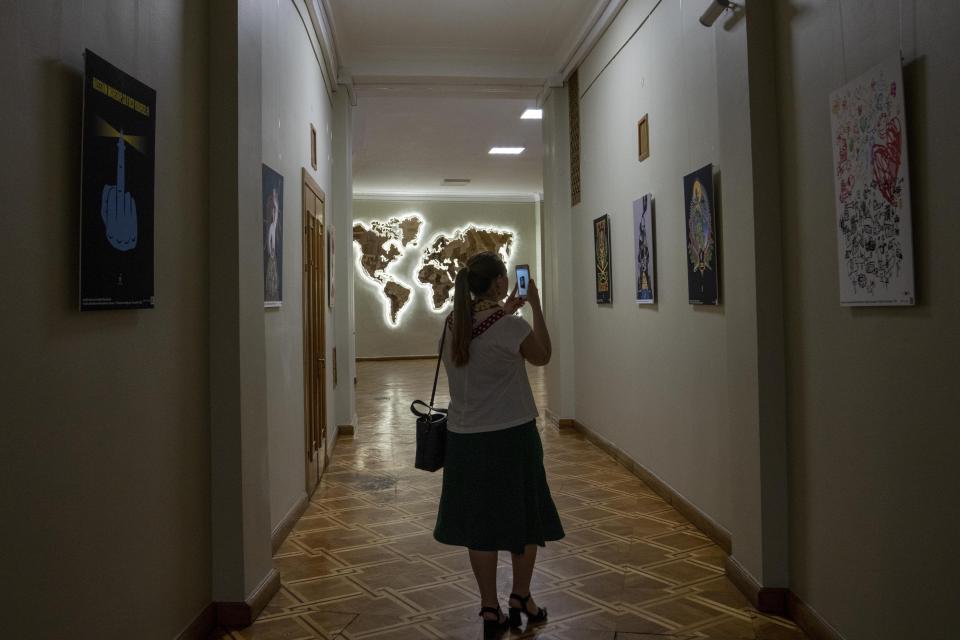 A woman takes photos during the opening of an exhibition dedicated to Ukrainian war art and posters, after a press conference given by Ukrainian Foreign Minister Dmytro Kuleba, at the foreign ministry, in Kyiv, Ukraine, Tuesday, June 28, 2022. (AP Photo/Nariman El-Mofty)