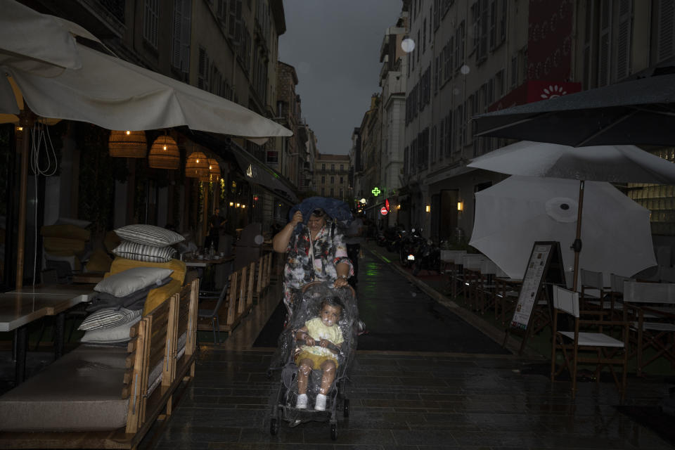 A woman pushes a baby stroller with a child covered with a plastic shield during a rainfall in Cannes, southern France, on Tuesday, May 24, 2022. (AP Photo/Petros Giannakouris)