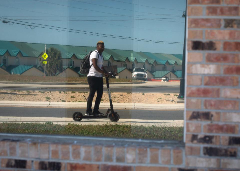 A person on a scooter rides by a storefront window near the roundabout on Front Beach Road in Panama City Beach.