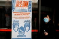 Woman wears a mask as she walks past a health warning poster at hospital, in Hong Kong