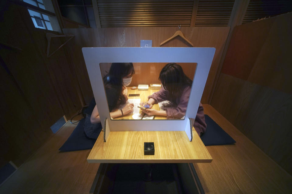 Customers order drinks and food with their phone through plastic protector against the new coronavirus infection at Kichiri, an "izakaya" restaurant chain in Tokyo Thursday, June 4, 2020. As Japanese return to schools, shops and offices reconfigured to help prevent new coronavirus infections with ample use of plastic screens, masks and reminders to keep their distance, access to faster testing is crucial, officials say.(AP Photo/Eugene Hoshiko)