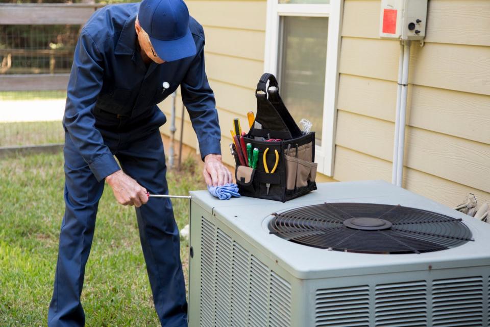 Repairman dressed in blue coveralls replaces dated outdoor air conditioning unit. 