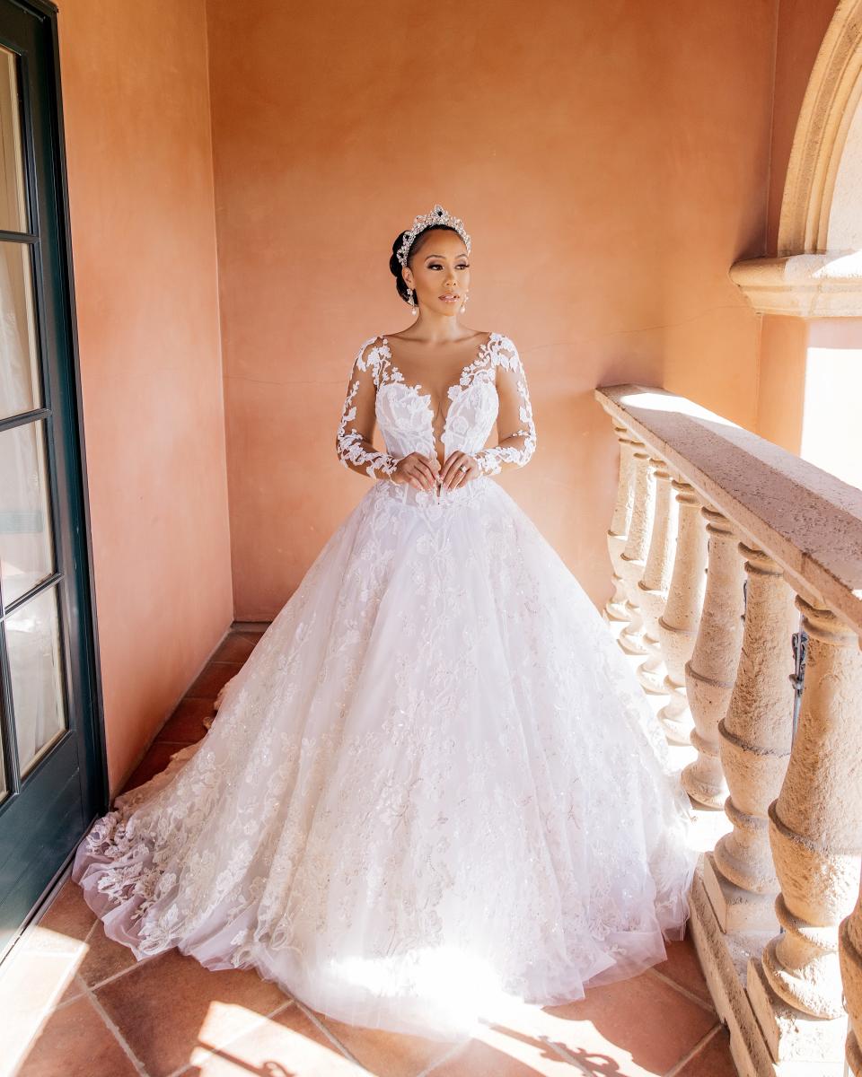 A bride stands on a balcony in a wedding dress.