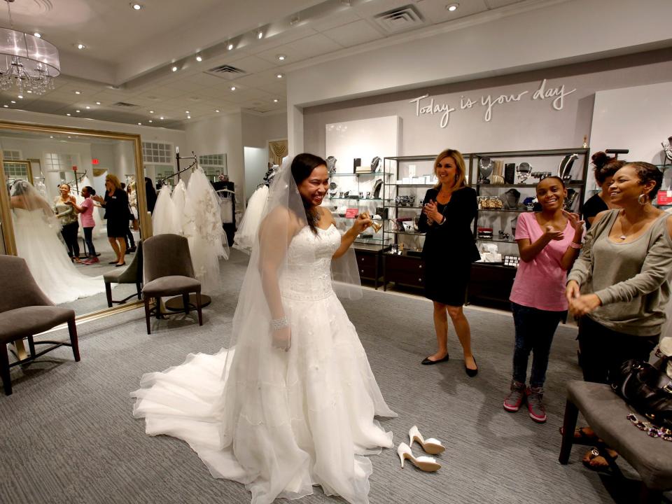 Woman wearing wedding dress and veil inside David's Bridal store surrounded by women