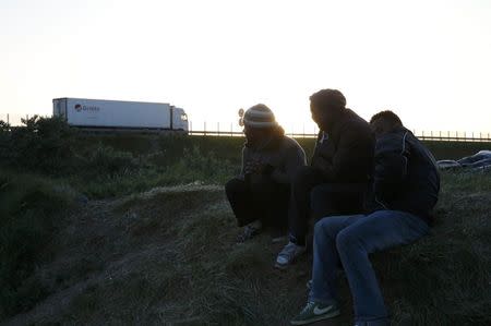 Migrants sit on an embankment near a road where trucks pass as they gather in Calais, France, May 18, 2015 after they travelled from the Mediterranean northwards in the hopes of crossing the English Channel on lorries and seeking asylum in Britain. REUTERS/Pascal Rossignol