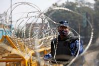 A member of the Rapid Action Force (RAF), wearing a protective face mask, is seen through barbed wire at the site of a protest against the newly passed farm bills at Singhu border near Delhi