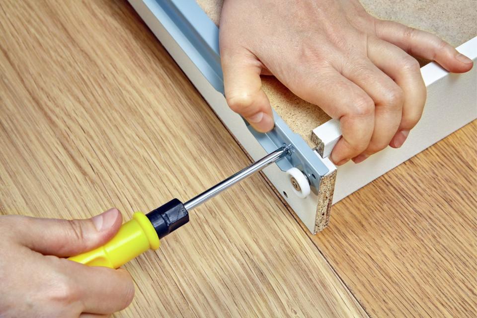 A close up of a pair of hands using a tool to assemble a piece of furniture.