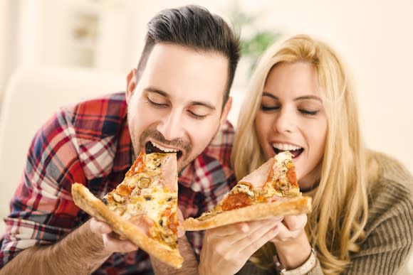 A man and woman taking bites out of pizza slices.