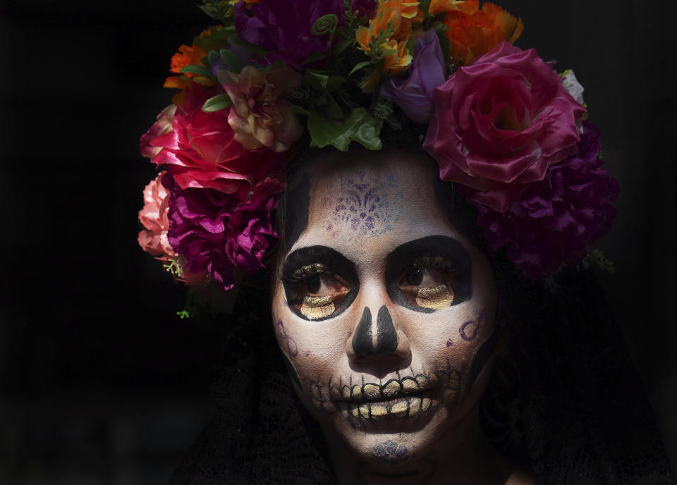 A woman dressed as Mexico's iconic "Catrina" poses for tourists in Mexico City's main square, the Zocalo, as part of the Day of the Dead festivities in Mexico City, Friday, Oct. 28, 2022. The holiday honors the dead as friends and family gather in cemeteries to decorate the graves of their loved ones. and hold a vigil during the night of November 1 and 2. (AP Photo/Marco Ugarte)