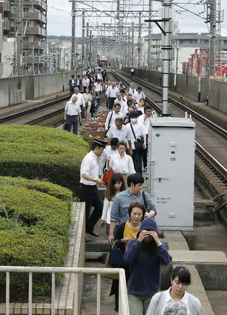 Passengers walk on a rail after their train was stopped in Ikdea, Osaka prefecture, western Japan, in this photo taken by Kyodo June 18, 2018. Mandatory credit Kyodo/via REUTERS
