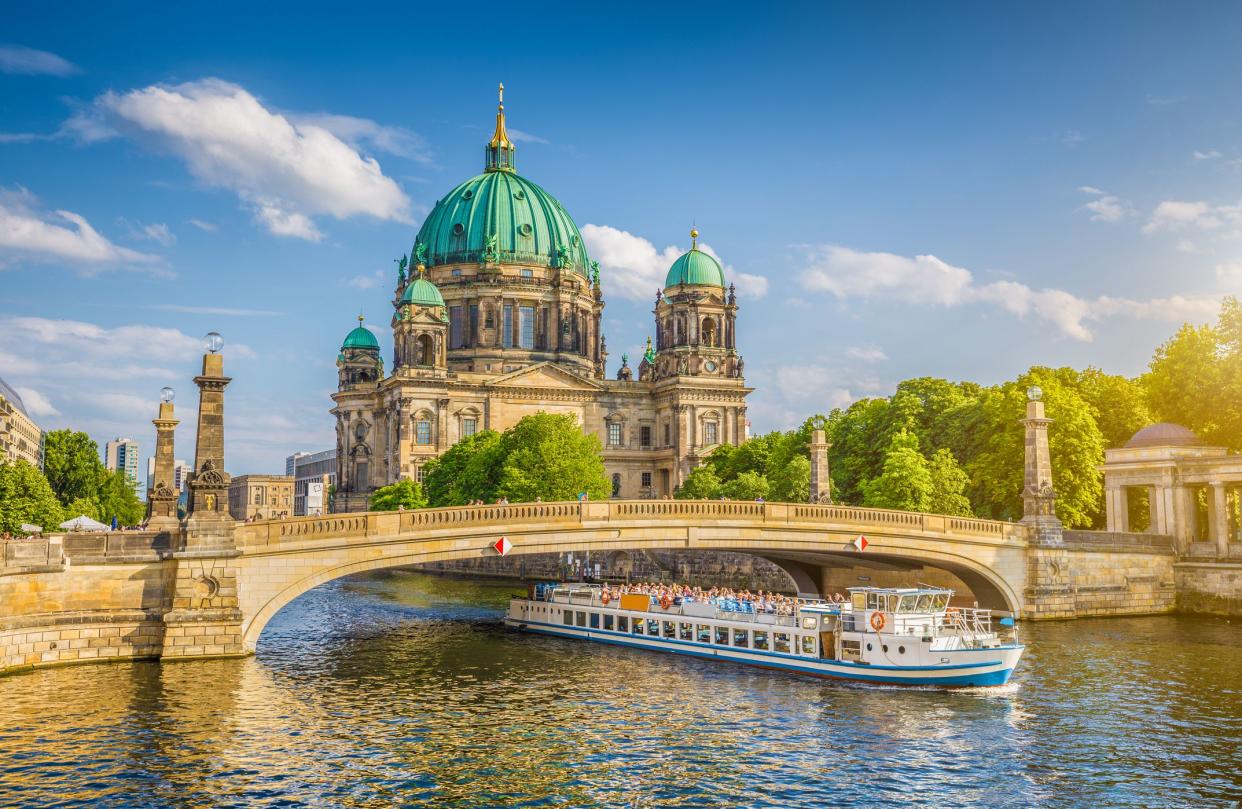 Beautiful view of historic Berlin Cathedral (Berliner Dom) at famous Museum Island with ship passing Friedrichsbrucke bridge on Spree river in golden evening light at sunset in summer, Berlin, Germany