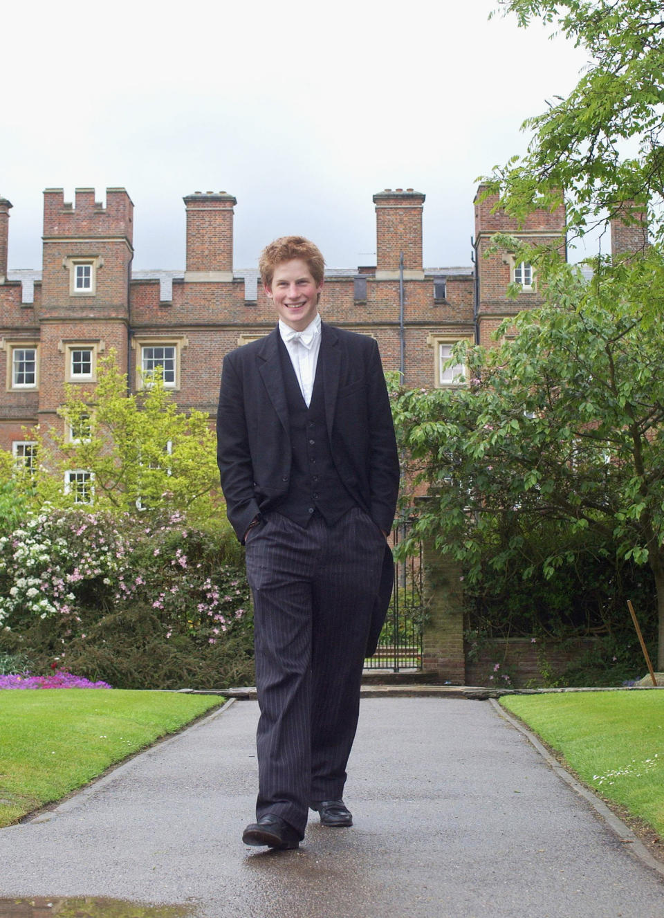 Prince Harry wearing his school dress, which consists of a black tailcoat, a waistcoat and pin-striped trousers, in March 2003. He has "stick-ups" (wing collars and a bow tie) because he is house captain of games.