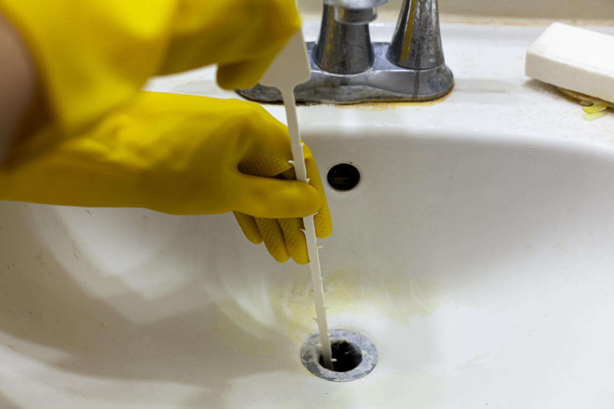 sink snake, A person is trying to unclog the drain of a sink using plastic disposable snake auger tool which helps pull hair and soap debris from the sinkhole. Close up DIY home maintenance concept.