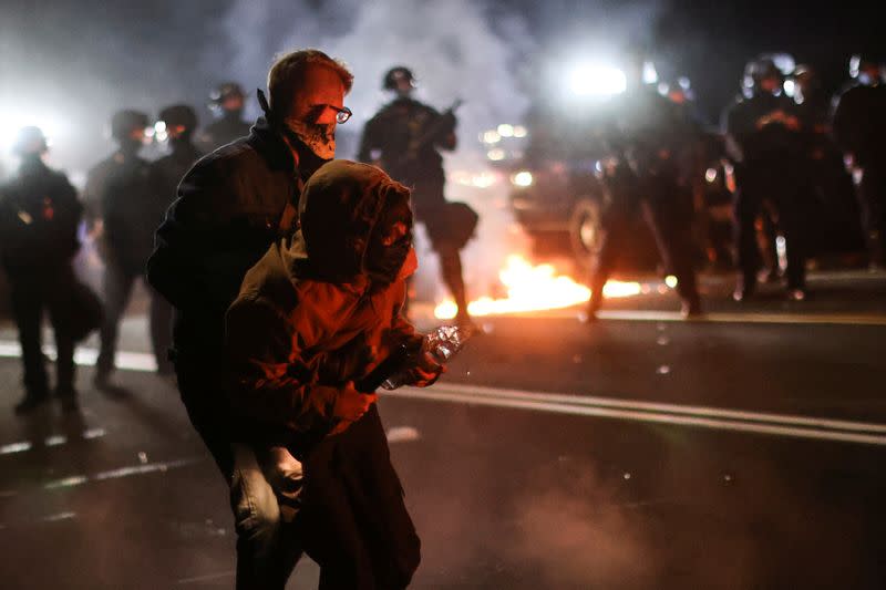 A protester is helped by another to retreat after clashing with the police on the 100th consecutive night of protests against police violence and racial inequality, in Portland, Oregon