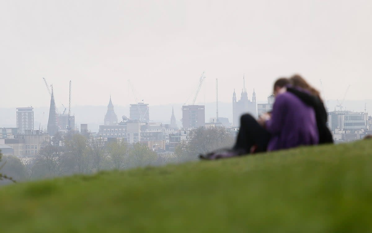 A couple sitting in Primrose Hill gazing at a smog-cloaked London skyline  (Philip Toscano / PA)