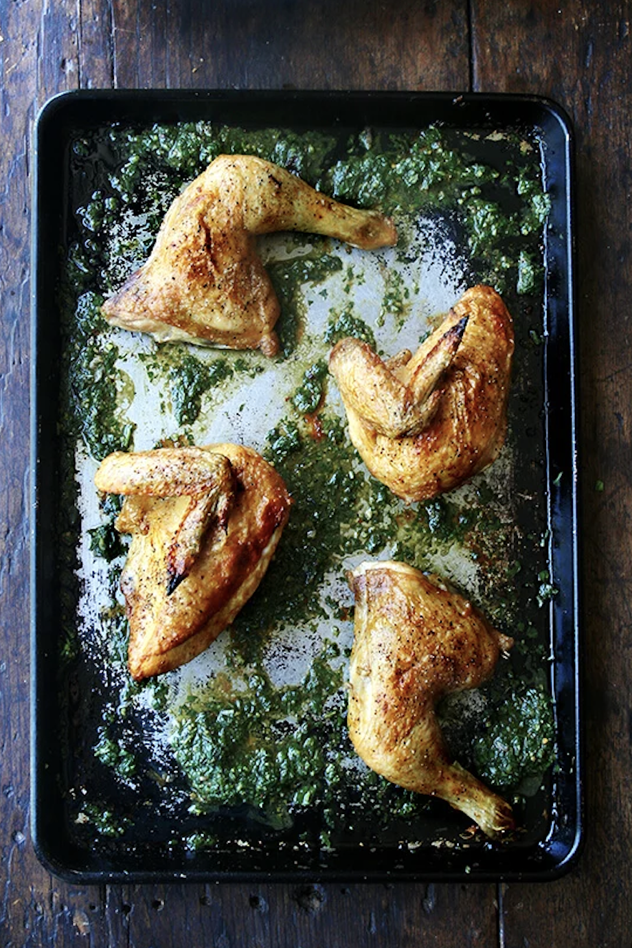 Four cooked chicken legs on a baking sheet, surrounded by chopped greens