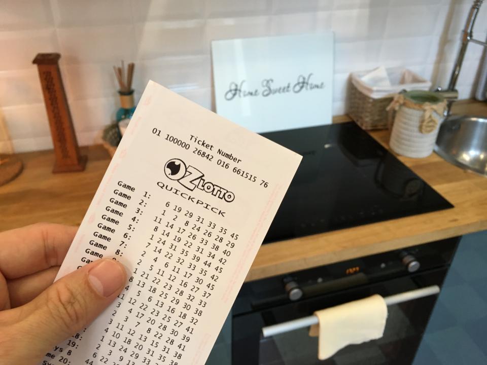 A man holds an OzLotto ticket in his kitchen