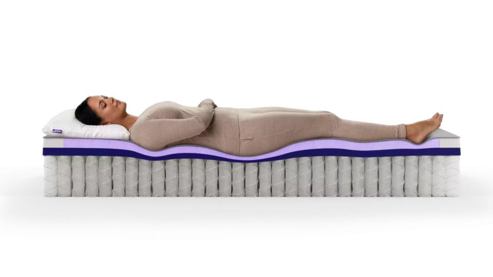 Brunette woman sleeps on the Purple Restore Hybrid Mattress with its internal layers exposed.