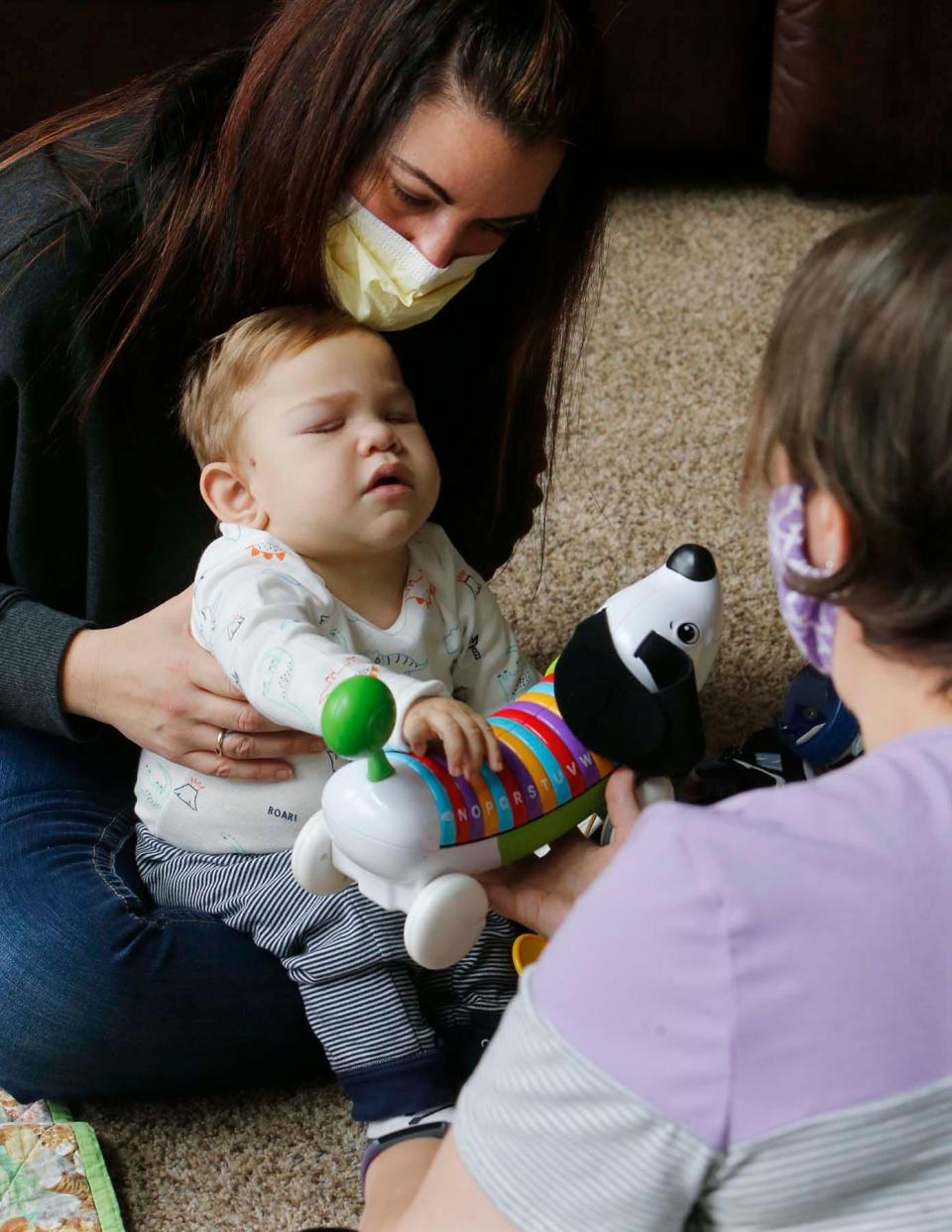 David Detwiler, 19 months, sits on the lap of his mother, Carlla Detwiler, as he reaches out to a toy dog during a session with physical therapist Jenn Masser on Nov. 11 at the Detwiler home in Massillon.