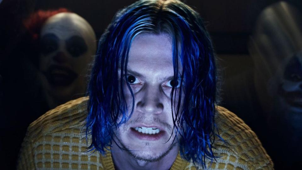 Evan Peters has blue hair and stares creepily into the camera flanked by a group of clowns in a still from American Horror Story: Cult.