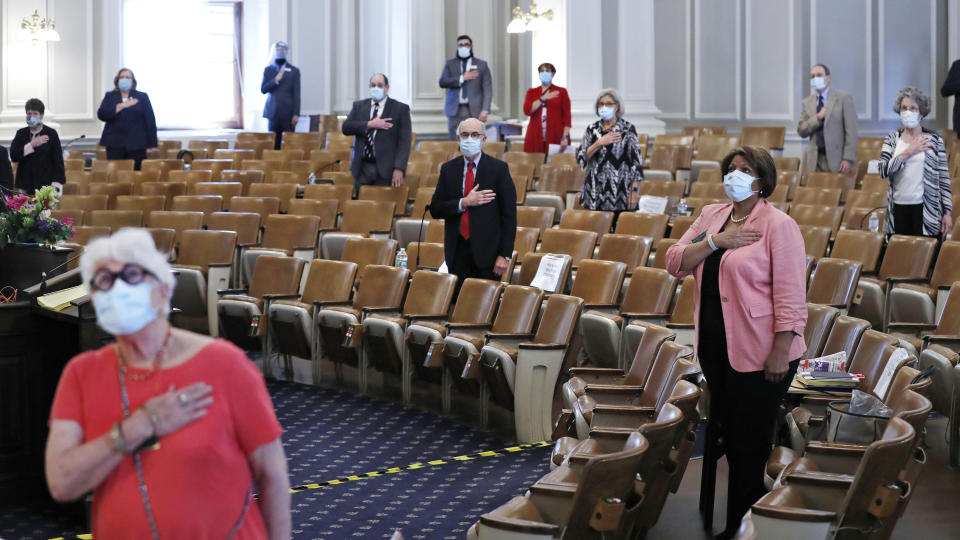 Members of the N.H. Senate stand for the Pledge of Allegience as they gather for a session on Tuesday, June 16, 2020 at the State House in Concord, New Hampshire. The 24 N.H. Senators met in the N.H. House Chamber while adhering to social distancing rules due to the COVID-19 virus outbreak. (AP Photo/Charles Krupa)