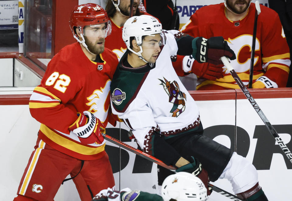 Arizona Coyotes forward Dylan Guenther (11) is checked by Calgary Flames defenseman Jordan Oesterle (82) during the second period of an NHL hockey game, Tuesday, Jan. 16, 2024 in Calgary, Alberta. (Jeff McIntosh/The Canadian Press via AP)