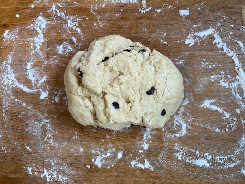 An overhead shot of pale scone dough dotted with sultanas turned out onto a wooden counter covered in flour.