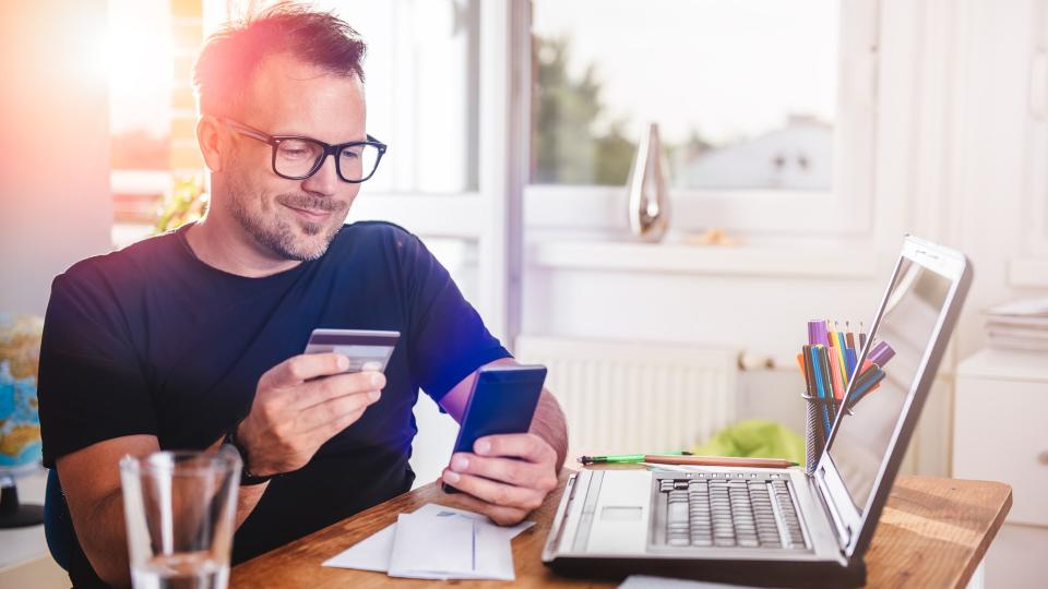 Man paying with credit card on smart phone at home office.