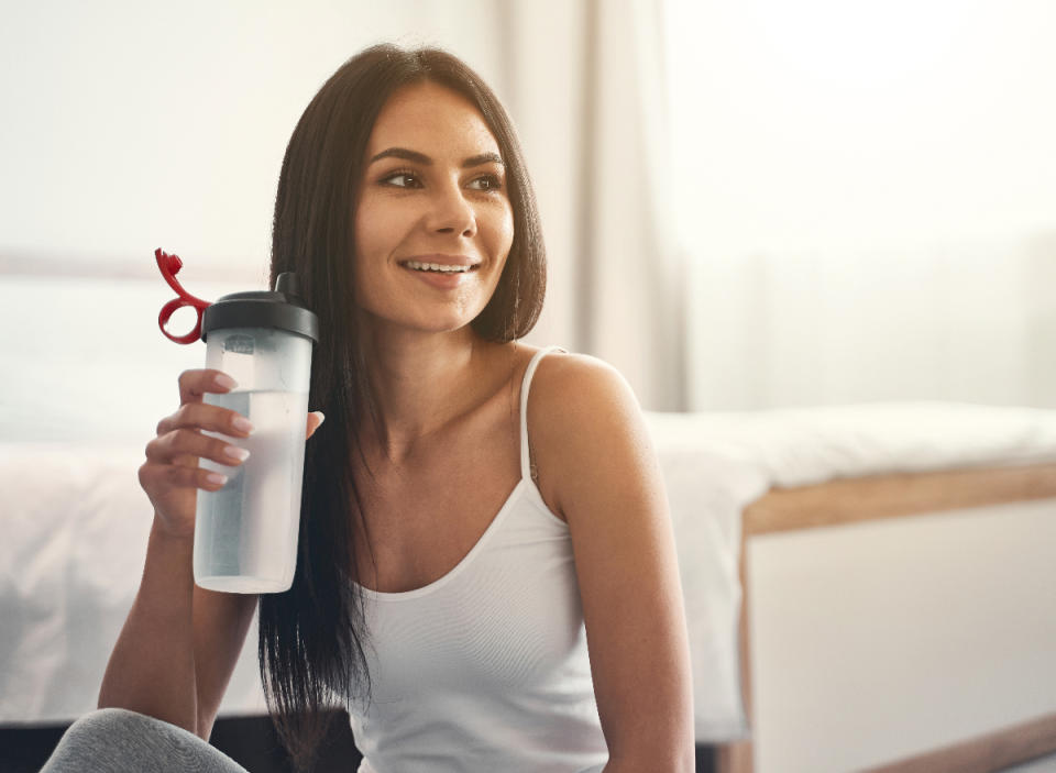 mujer bebiendo una botella de agua en un dormitorio luminoso, concepto de cómo quemar calorías mientras ve la televisión
