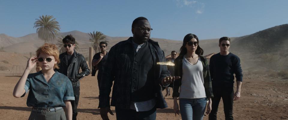 A still from Eternals shows Brian Tyree Henry as Phastos, Gemma Chan as Sersi, Richard Madden as Ikaris, Lia McHugh as Spike, and Barry Keougn as Druig walking through the desert